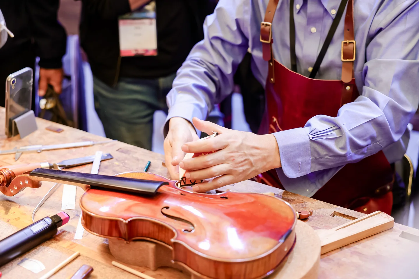 Demonstração de trabalho em um violino durante a Music China 2025 Mãos de um profissional trabalham sobre um violino em uma bancada de luteria.