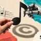 Mão humana e mão robótica seguram a mesma nota musical, com sombra em forma de copyright e logotipo do Suno